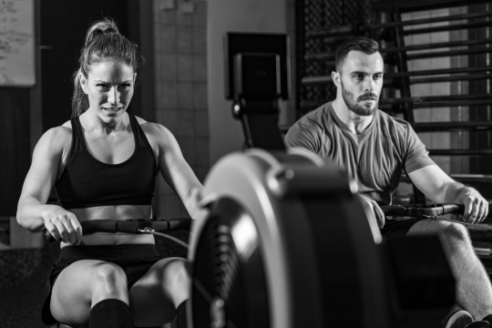 Man and woman using rowing machine and exercising in a gym