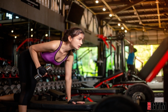 Female in gym leaning on training bench holding dumbell