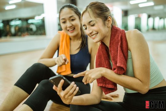 two females in a gym looking at their phone in studio