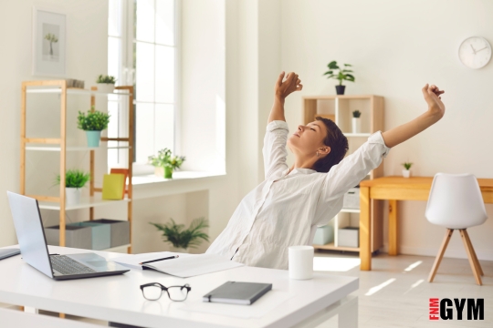 Female sitting at a desk in light and airy office stretching arms above the head