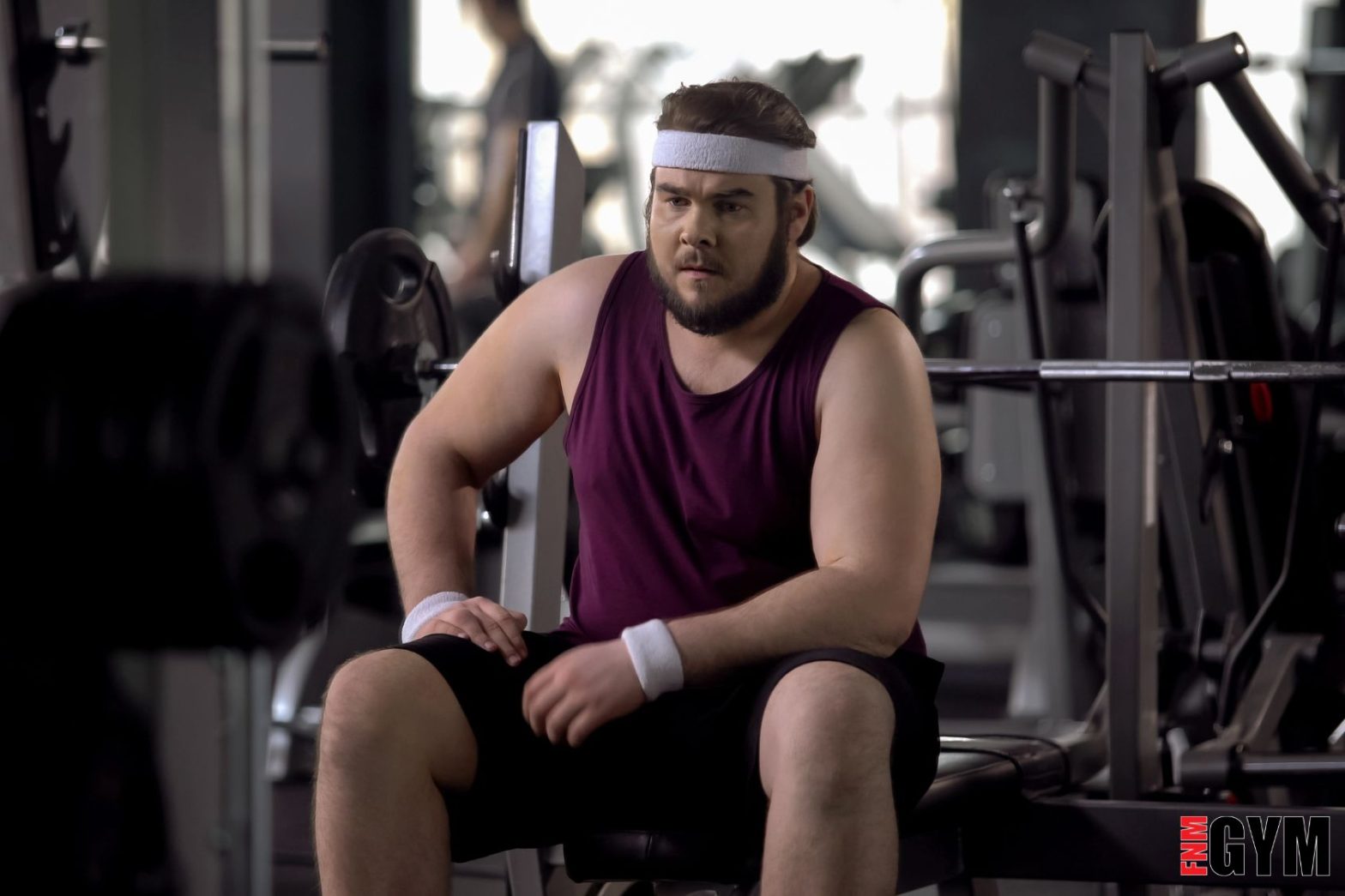 Male wearing purple top and sweat band sitting on bench
