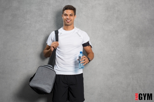 Male in white t-shirt holding gyn bag and bottle of water