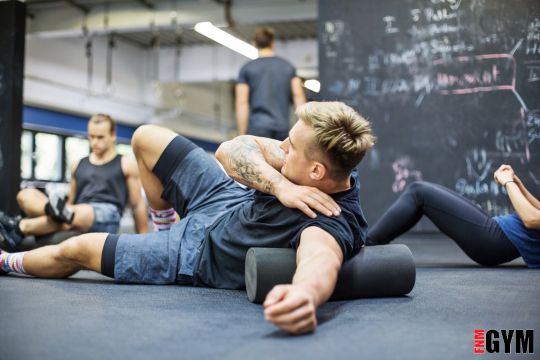 male wearing blue short and black top laying on floor with roller