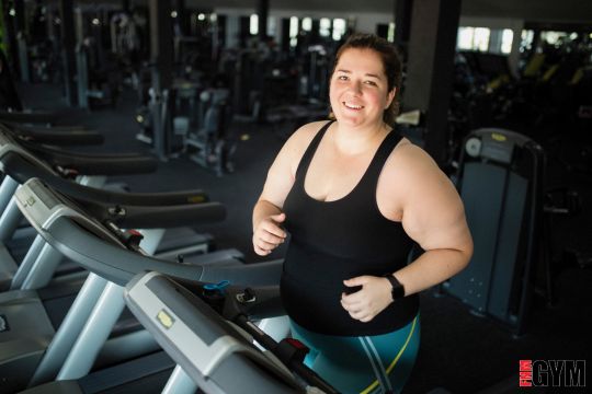 Female with dark hair wearing black top smiling and walking on treadmill