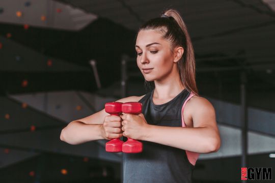 female in black top holding red dumbbells at chest