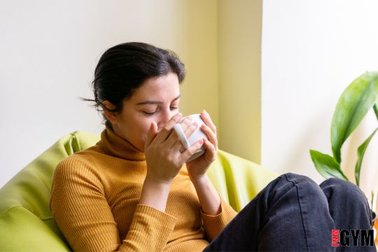 female in yellow top sitting on couch with hot drink